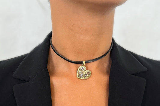 Brass necklace with a heart-shaped pendant worn by a person against a plain background