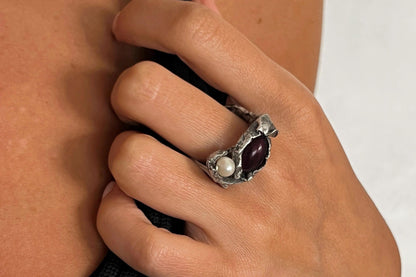 Close-up of a hand wearing a silver ring with a garnet and pearl