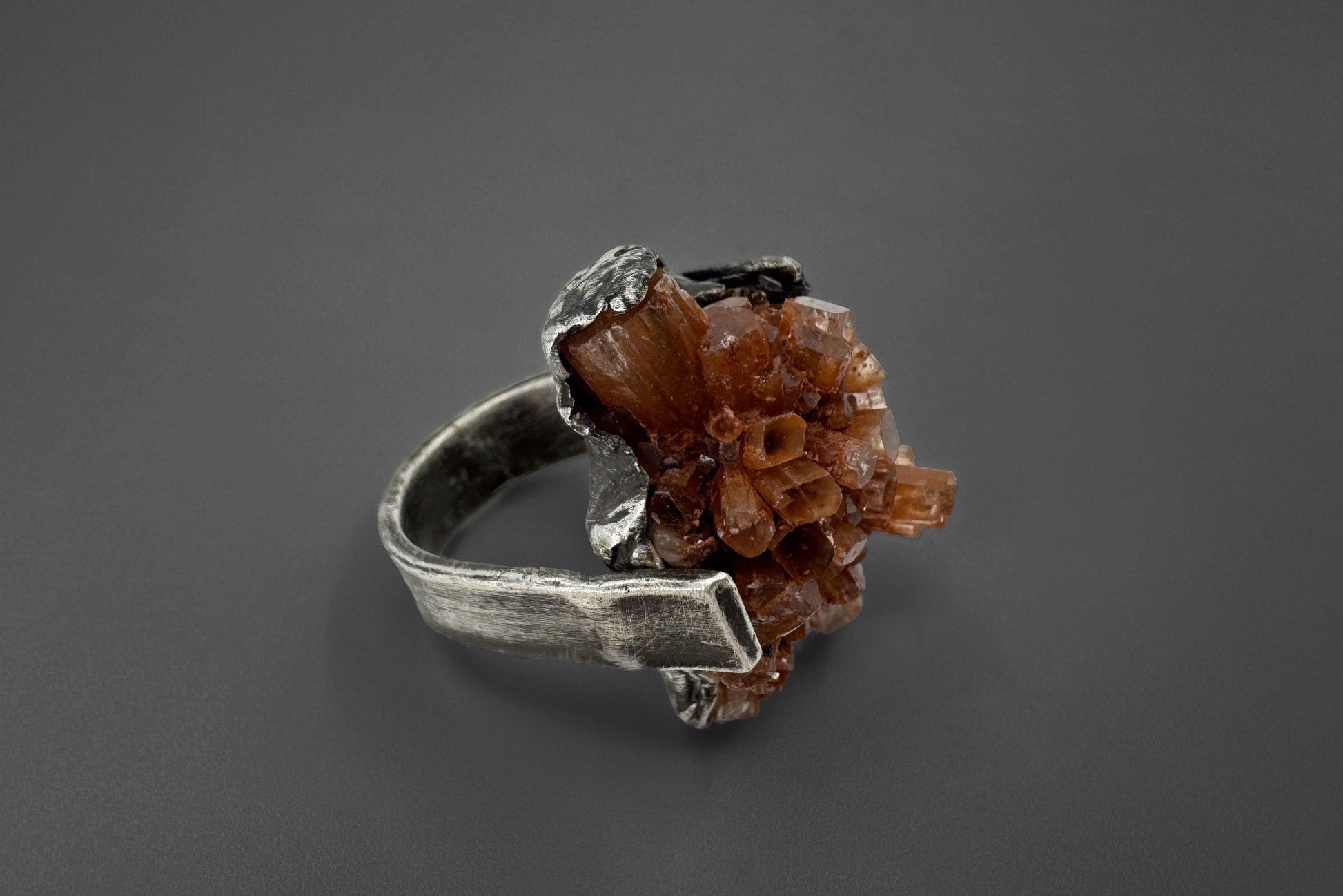 Silver ring with a brown aragonite crystal on a dark gray background