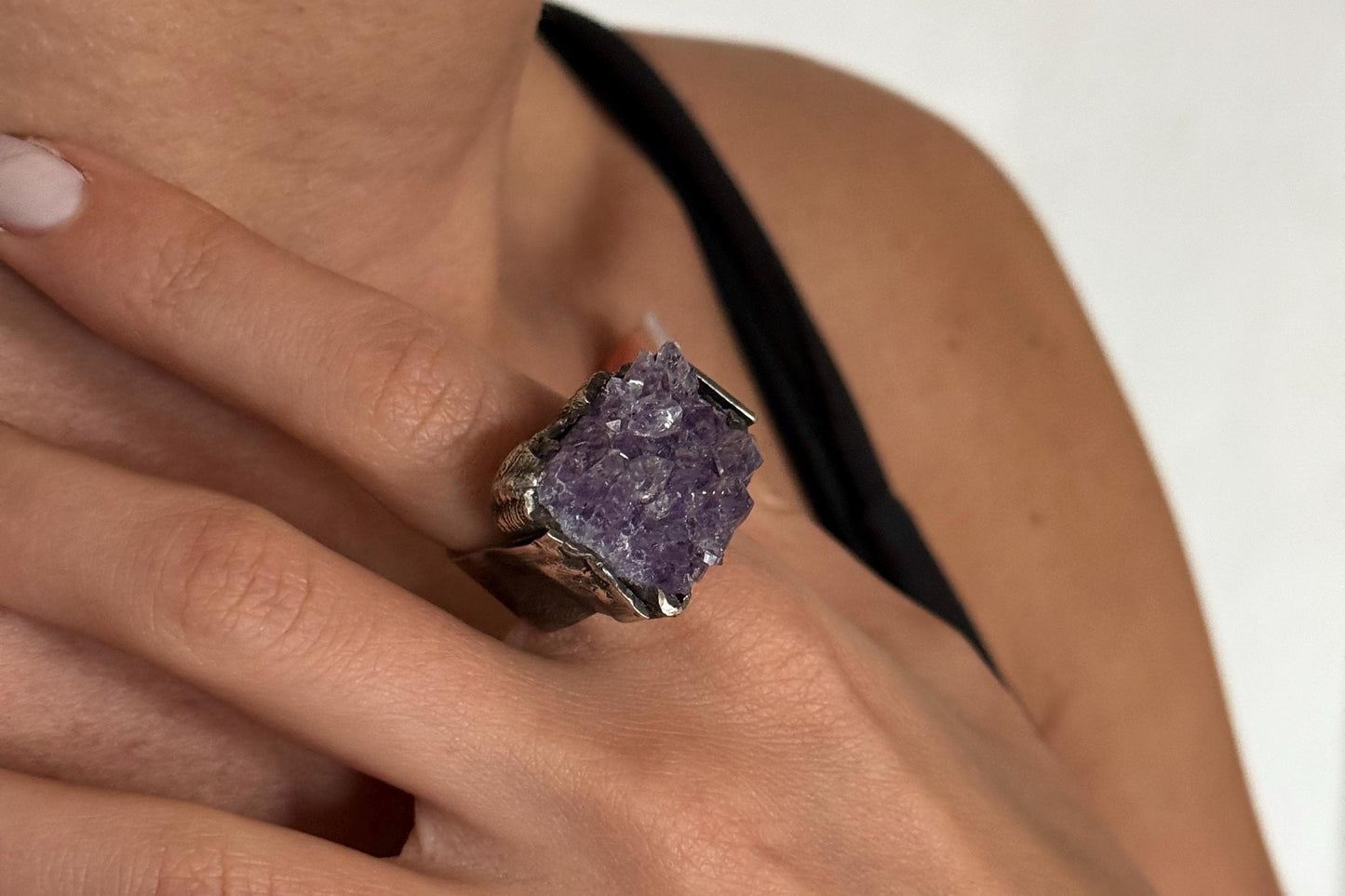 Close-up of a hand wearing a ring with a purple amethyst gemstone on a white background